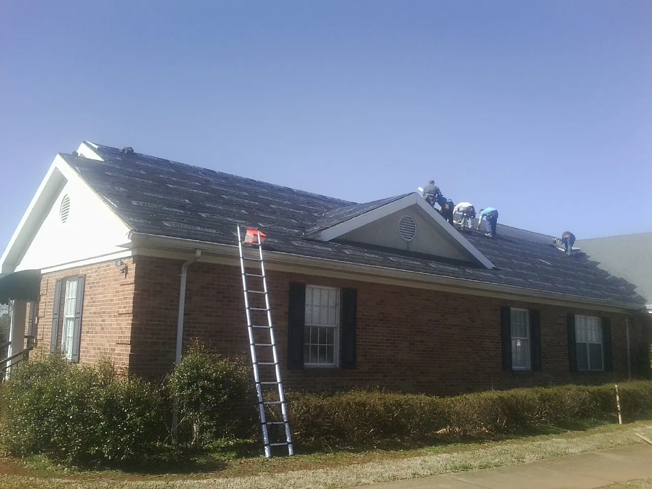 Crew tearing shingles off a brick ranch roof with a ladder set — Emergency Roof Repair work by our crew in Loxahatchee
