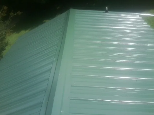 New green metal panels meeting at the ridge of a roof — Flat Roof Repair work by our crew in Loxahatchee