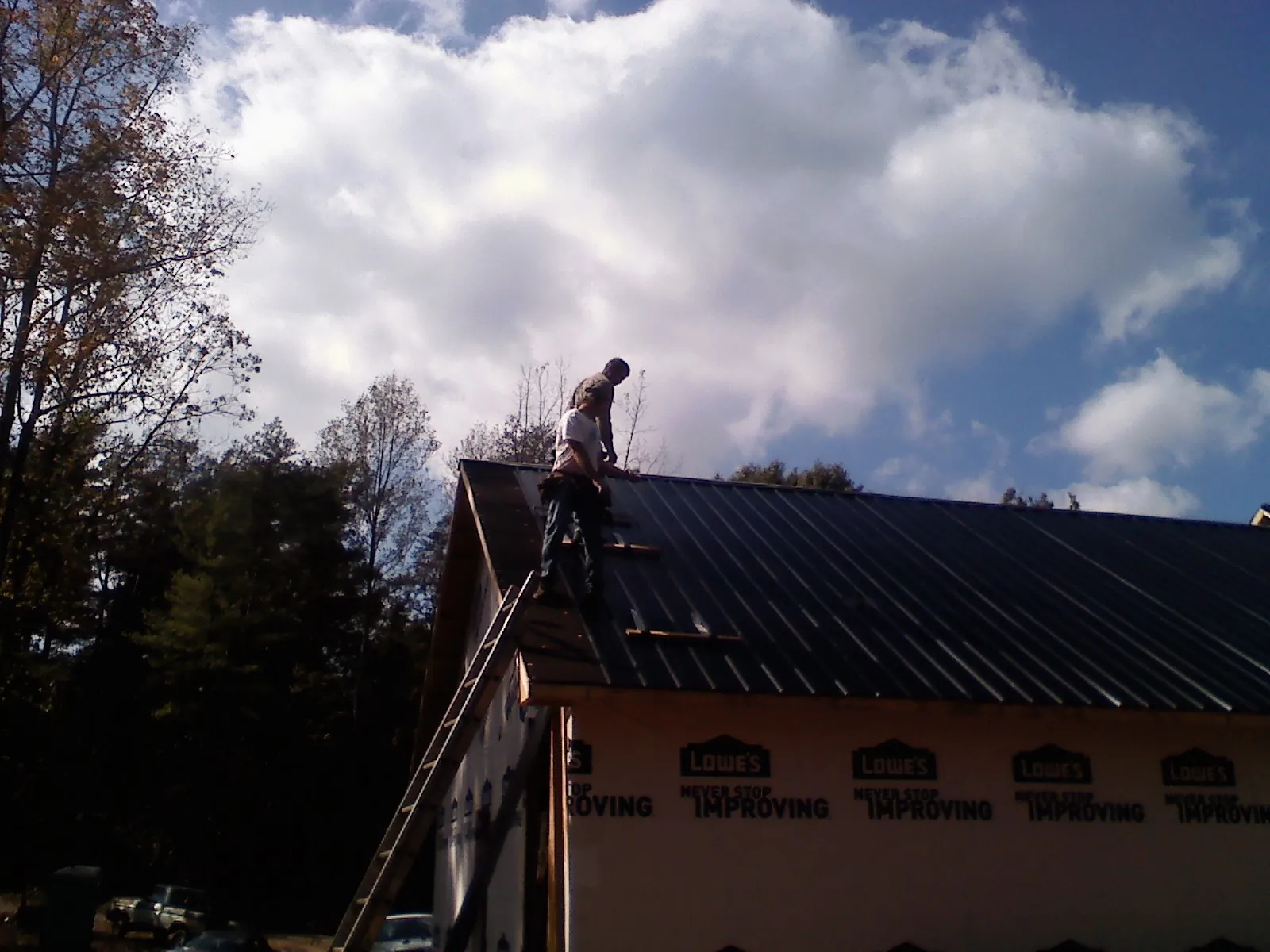 Roofer fastening dark metal panels high against a cloudy sky, from a Roof Inspection job in Loxahatchee