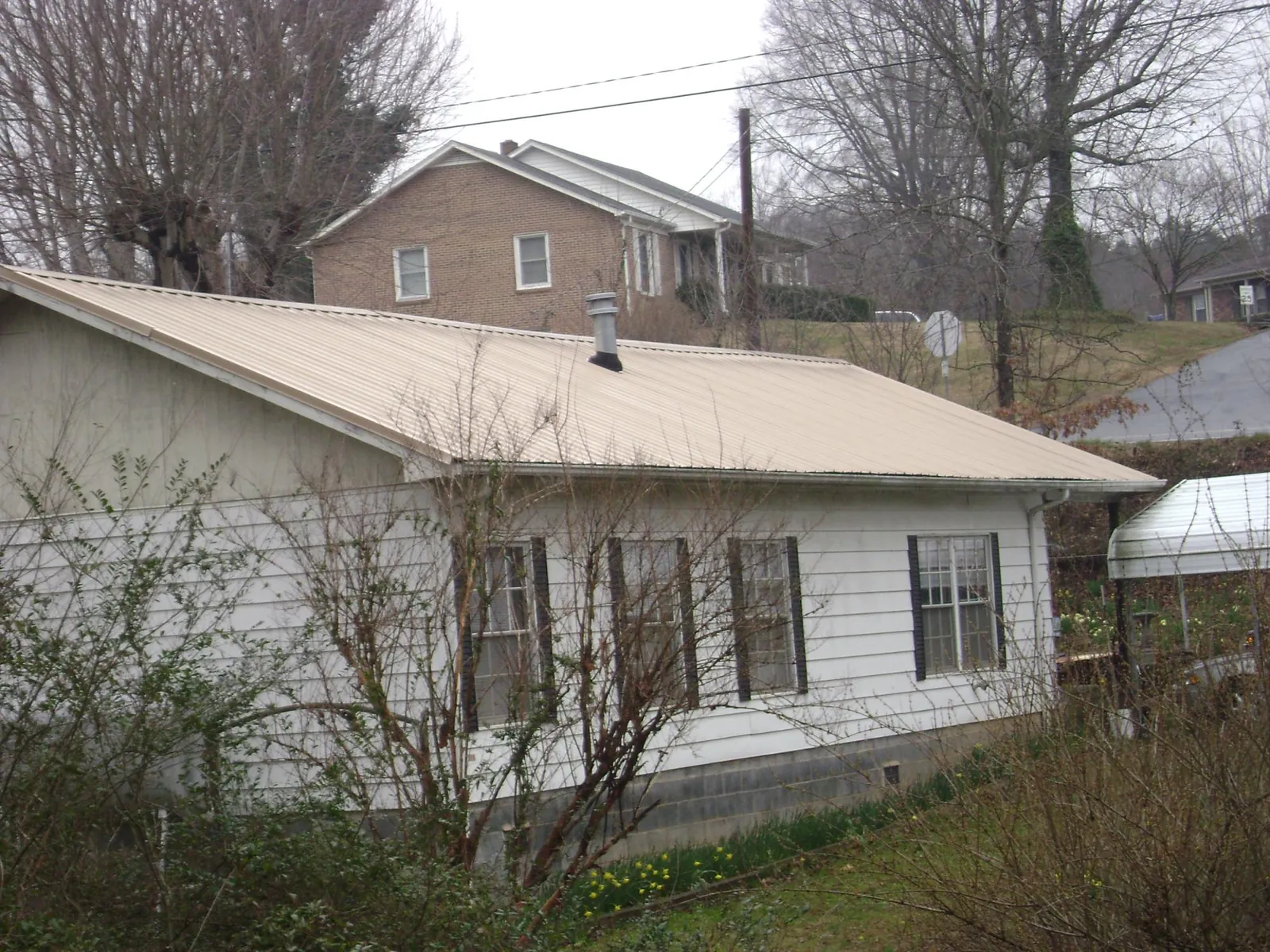 Tan metal roof on a white sided house set into a hillside — Commercial Roofing by Roofing Brothers in Loxahatchee