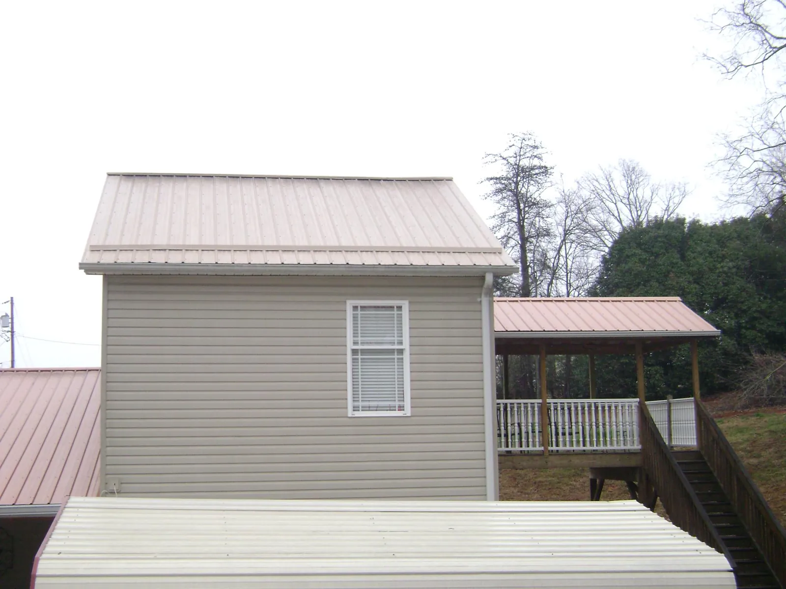 Tan metal roofs on a two story addition and attached porch, from a Roof Replacement job in Loxahatchee